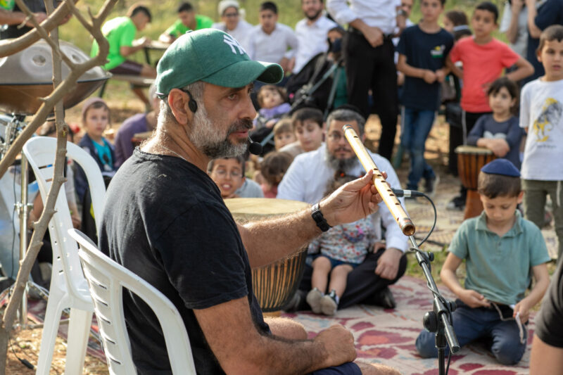 מנחה מדגים חליל לילדים בפעילות מוזיקה בחוץ